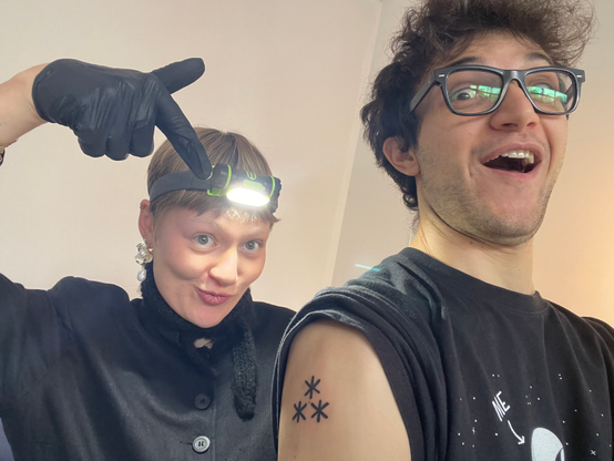 Selfie of Feine with tattooing gloves and a headlamp + me with the asterism just tattooed on my shoulder