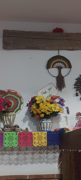 Es un altar del día de los muertos decorado con flores y vivos colores como  en México y pone in cartel" haz por venir"