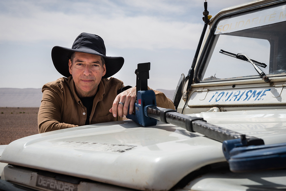 Television host and science writer Geoff Notkin leans across the hood of a vintage Land Rover in the Sahara Desert