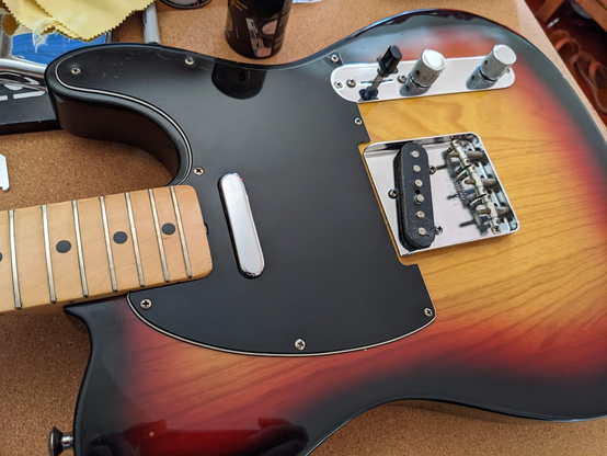 A shot of a fender telecaster guitar in sunburst finish with a black pickguard and silver/chrome hardware.