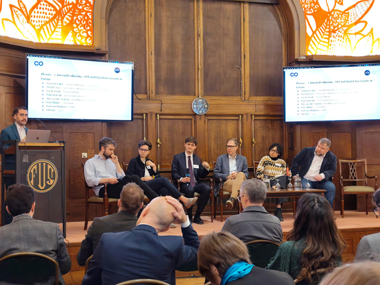 Photo of a panel of speakers in an old style wooden room with Felix Hlatky in the middle dressed in suit and tie.