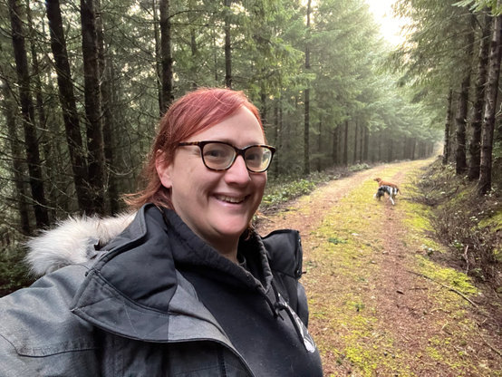 A red-haired middle-aged woman wearing a winter coat goes for a walk along a logging trail in the winter with her dogs. 